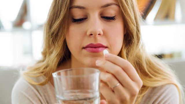 Portrait of young woman taking pills at home.