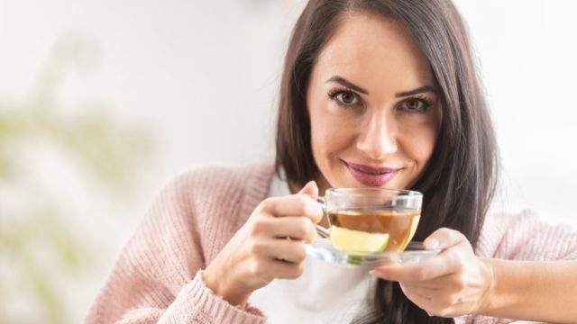 Woman looks into camera while drinking tea with lemon.