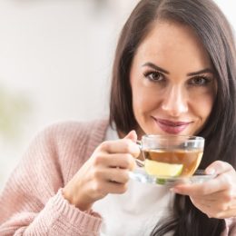 Woman looks into camera while drinking tea with lemon.