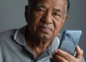 Unhappy elderly man thinking while using smartphone in studio and looking at camera. old man with sad face