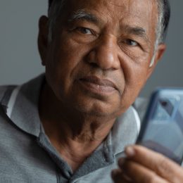 Unhappy elderly man thinking while using smartphone in studio and looking at camera. old man with sad face