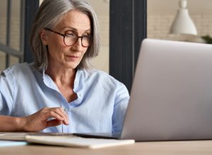 Mature adult 60s aged woman working at laptop watching video conference