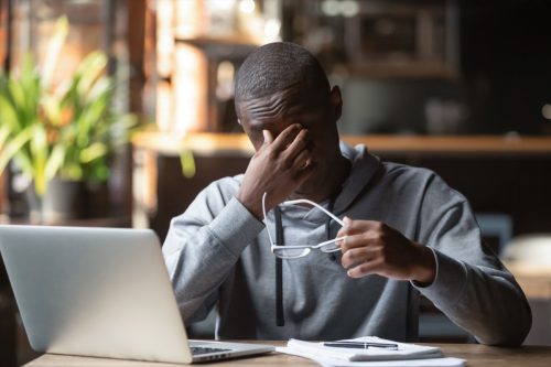 Tired stressed black guy take off glasses feel eye strain after computer work study in cafe, overworked african american business man student suffer from bad blurry vision sight problem sit at desk