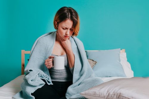 Woman sore throat with glass of water in her bed. Blue background