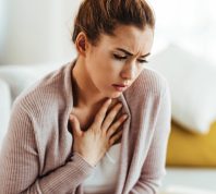 Young woman feeling sick and holding her chest in pain at home.
