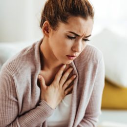 Young woman feeling sick and holding her chest in pain at home.