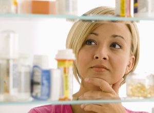 A young woman is looking through her medicine cabinet.