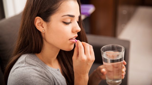 Woman taking a pill with a glass of water at home.