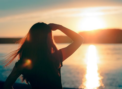 Happy Hopeful Woman Looking at the Sunset by the Sea. Silhouette of a dreamer girl looking hopeful at the horizon