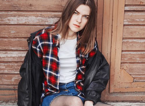 Portrait of a woman in rock, grunge style. Filmed on the street, in the open space. Dressed in a black leather jacket, shirt in red plaid. Street style and fashion.