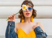 beautiful sexy woman in yellow stylish dress wearing denim jacket, holding flower, trendy outfit, hippie indie style, spring summer fashion trend, blue sunglasses, street fashion, trendy accessories