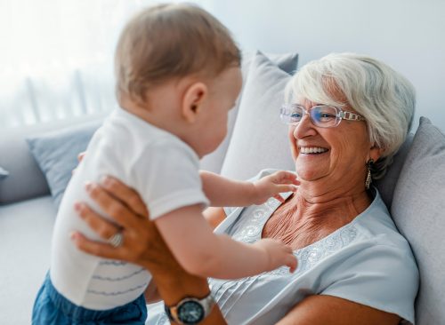 Little boys are just superheroes in disguise. Grandmother looking at baby boy with smile. Proud grandmother playing with grandson. Woman with baby grandson