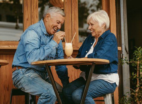 Cheerful old couple sitting at cafe having a coffee. Senior man and woman sitting at restaurant table talking with cold coffee on table.