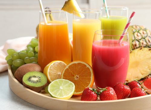 Wooden tray with glasses of different juices and fresh fruits on table