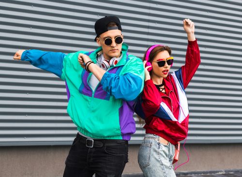 Back in time 90s 80s. Stylish young man in a retro jacket and a girl in red and with a vintage cassette player, against a steel wall, fashion trends, a street image