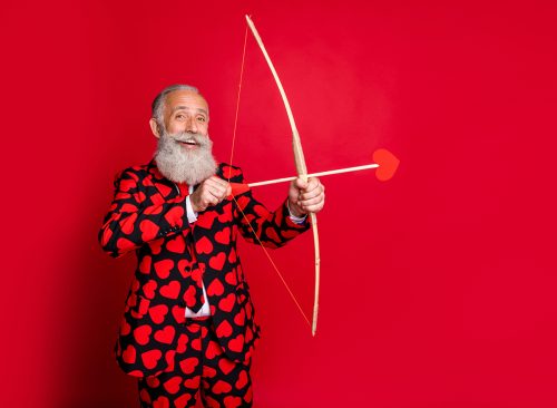 Portrait of his he nice attractive cheery trendy white-haired guy shooting arrows wedding match maker soulmate finding date isolated on bright vivid shine vibrant red color background