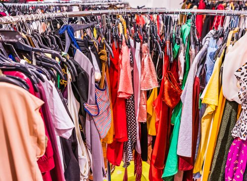 Crowded clearance section in a clothing store, with various colorful garments placed tightly on racks in no particular order; fast fashion concept