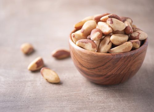 Brazil nuts in wooden bowl on wood textured background. Copy space. Superfood, vegan, vegetarian food concept. Macro of brazil nut texture, selective focus. Healthy snack.