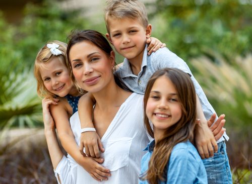 Portrait of a nice young mother with pleasure spending time with her three precious kids in the spring park, having fun together, big happy family enjoying life