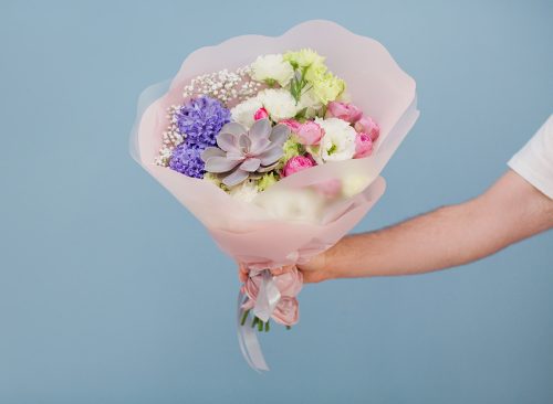 Delivery man in white t-shirt with beautiful bouquet on a blue background. Flowers delivery concept. Banner with man with flowers
