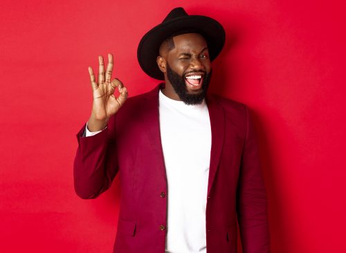 Christmas shopping and people concept. Handsome Black man showing ok sign with confidence, give guarantee, saying yes, standing over red background