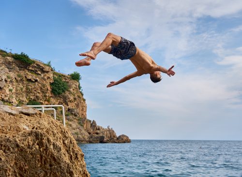 Freedom, motivation and creativity, man flipping from the scale on the beach. Young man doing a back flip into sea, Antalya, Turkey