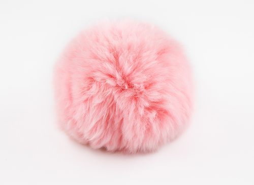 A fluffy ball of pink faux fur on a white background. Pompon. A toy for a cat. Decoration and decor of clothes. Eco-fur ball, soft and pleasant to the touch