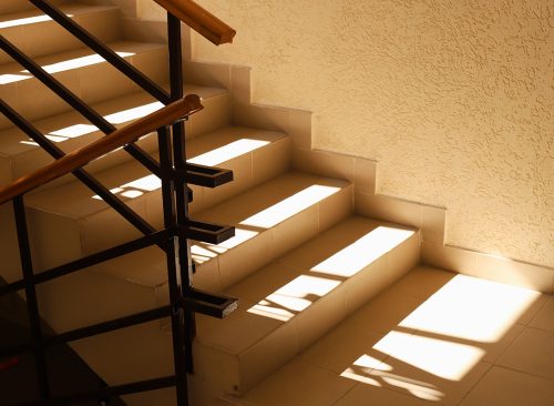 Sunlit staircase with railings in the house. Staircase at the entrance of an apartment building. Modern entrance interior in living complex. Shadow and light.