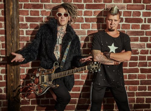 Two punk rock musicians in concert costumes posing with an electric guitar near a brick wall. Youth alternative culture. Grunge style.