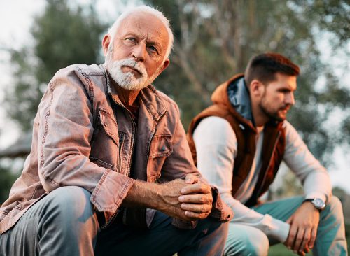 Pensive senior father ignoring his adult son after an argument in nature.