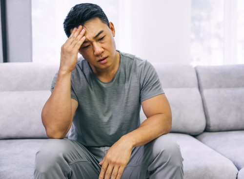 Feeling stressed. Frustrated handsome young man touching his head and keeping eyes closed while sitting on the couch at home