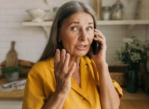 Attarctive retired female gesticulating with anxiety talking on phone, having worried face, using smartphone for conversation wih bank, trying to solve problem with savings account