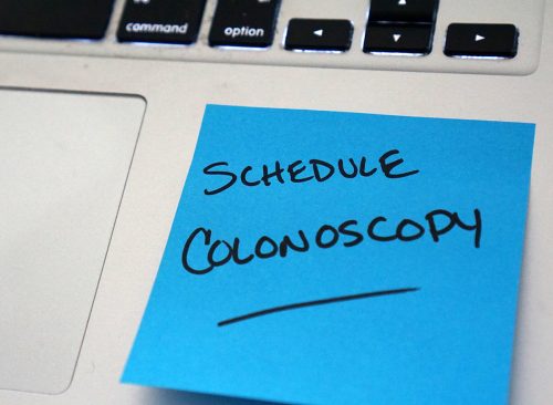 Sticky note reminder on laptop to schedule a colonoscopy
