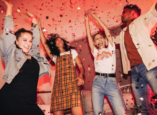 Friends having fun at a house party. Group of cheerful friends dancing to their favourite song under falling confetti. Multicultural friends enjoying their weekend together.