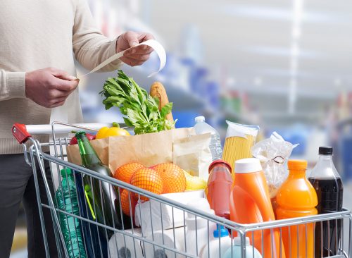 Man standing next to a full shopping cart and checking the grocery receipt