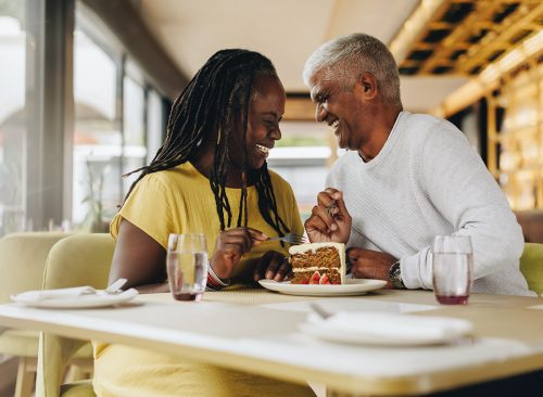 Happy mature couple laughing cheerfully while sharing a delicious cake in a cafe. Carefree senior couple having a good time in a restaurant. Mature couple enjoying their retirement together.