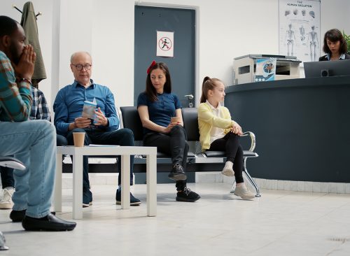 Many patients sitting in waiting area lobby at hospital reception, preparing to start checkup visit with appointment. Mother with child, senior man and other people in waiting room. Tripod shot.