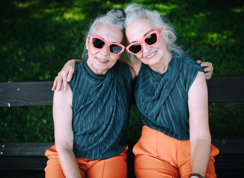 High angle view of happy senior women, twins in same clothes, smiling and posing in city park.