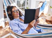 Middle age hispanic couple reading book lying on hammock at terrace