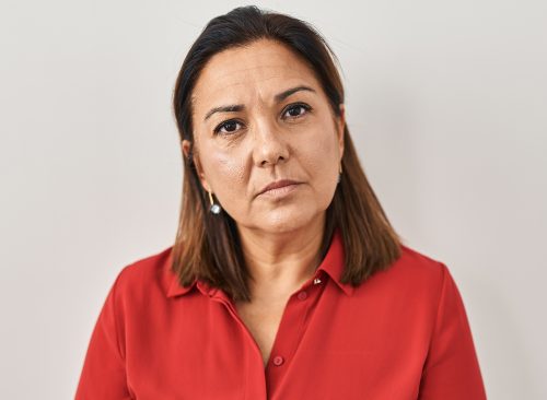 Hispanic mature woman standing over white background relaxed with serious expression on face. simple and natural looking at the camera.