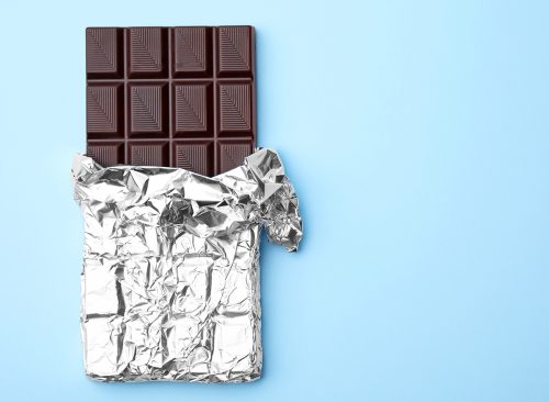 Tasty chocolate bar on light blue background, top view. Space for text