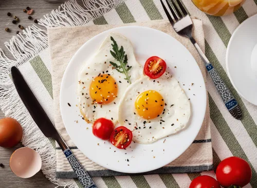 Fried eggs for breakfast. Healthy breakfast with vegetables and herbs. Fried eggs on a white plate. Serving on the table. Morning fried eggs with coffee and orange juice.