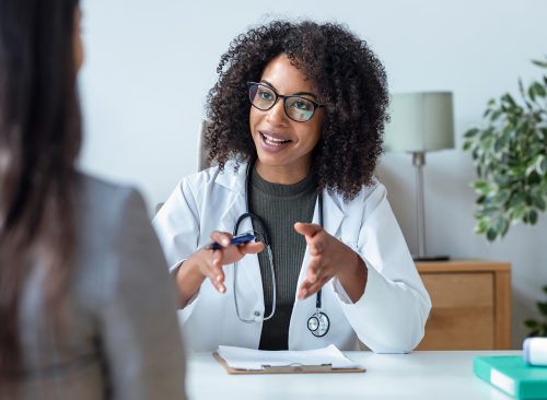 Shot of beautiful cheerful female doctor talking while explaining medical treatment to patient in the consultation.