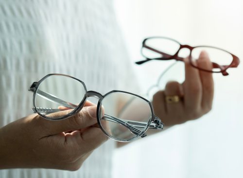 Close-up of a female hands client showing two glasses, making a choice. Blurred background, selective focus on eyewear
