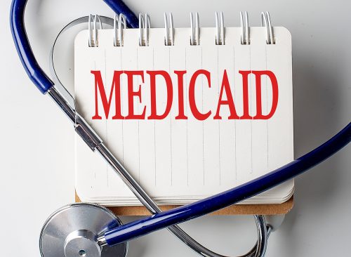 MEDICAID word on a notebook with medical equipment on background