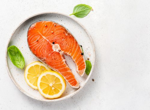 Fresh raw salmon steaks with spices, lemons and pink salt on white plate. Top view of fish with copy space. Keto recipe.