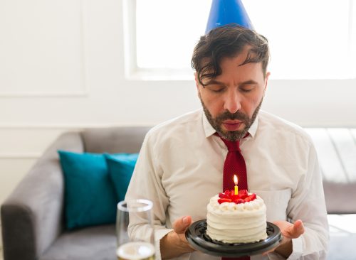 Sad caucasian man blowing his birthday candle on a cake and celebrating his birthday alone looking sad and depressed