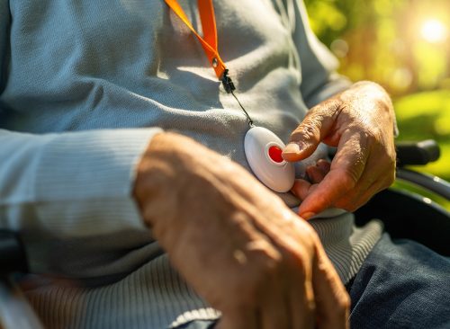 Senior man pressing Alarm Button in a wheelchair outside in a park, closeup. Emergency call system concept image.