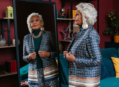 Stylish senior woman trying on fashionable clothes while looking at the mirror at home