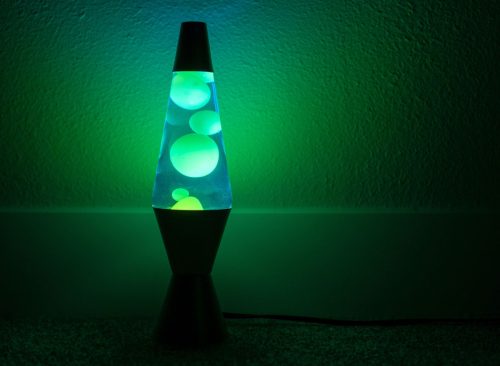 Green lava lamp stands near a white wall in the darkness
